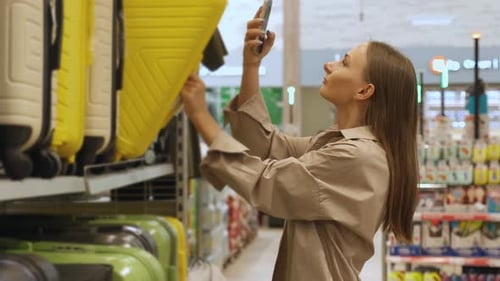 A Woman is Shopping for a Suitcase in a Retail Store She Reaches Out to Select a Suitcase From a