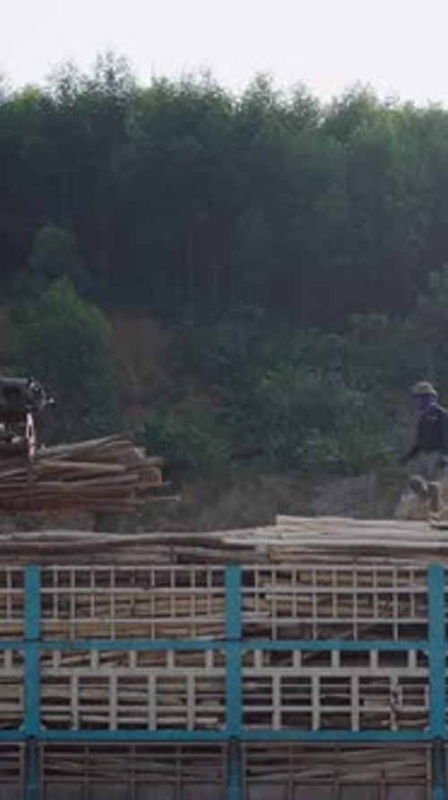 Asian Worker on Top of a Truck Bed Guiding the Crane Driver As They Load a Truck in Vietnam