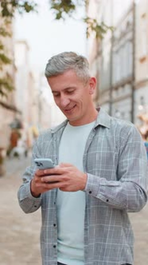 Happy Caucasian Man Using Smartphone Typing Text Messages Browsing Internet Standing on City Street
