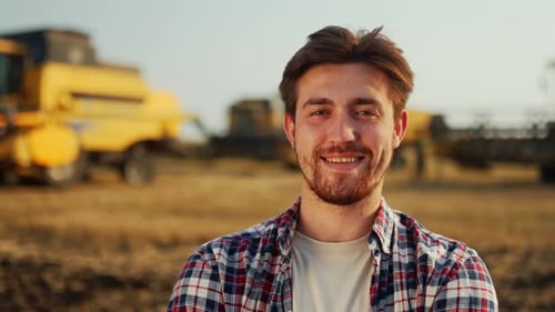 Portrait of Proud Farmer with Hands Crossed on Chest in Harvested Wheat Field Harvester Machine