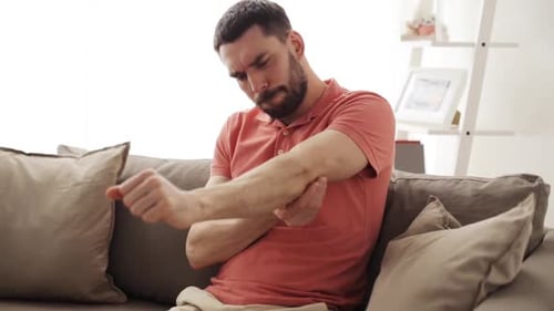 Man Massaging Sore Elbow on Couch Indoors
