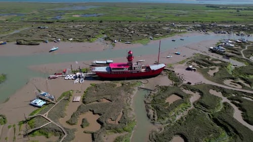 Bright red Tollesbury lightship boat moored on Essex marina marshland aerial orbiting view