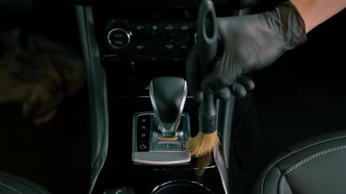 Car wash worker thoroughly cleaning the interior of a luxury car with a brush, gear box, detailing