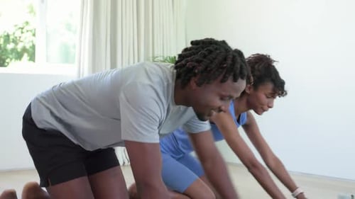 Pareja chocando los cinco para comenzar el entrenamiento arrodillada en casa sobre colchonetas verdes, bajando para hacer flexiones