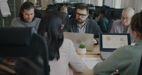 Businessman Talking to Group of Employees Discussing Work Sitting Around Table in Office