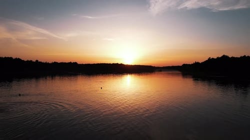 Aerial View of a Beautiful Orange Sunset at the Lake and Dark Silhouettes of People on the Sandy