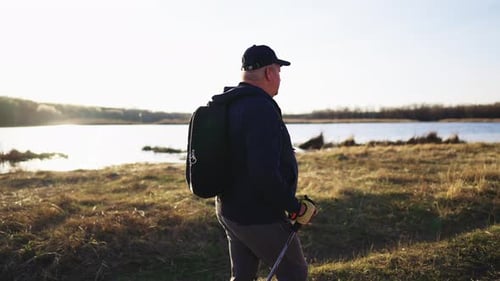 Active Handsome Elderly Man with Nordic Walking Sticks Walks Forward Through Along the Lake at