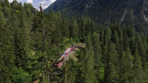 Aerial Shot of Red Rhaetian Railway Train Crossing a Mountain Forest