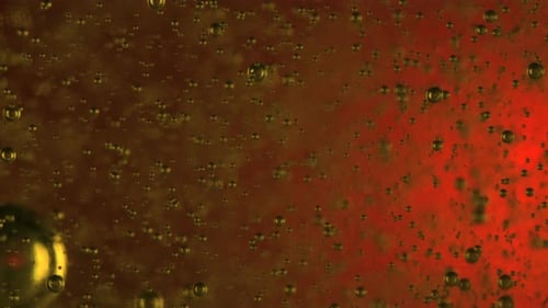 Pequenas bolhas em textura de gel se movendo contra fundo vermelho iluminado. Macro