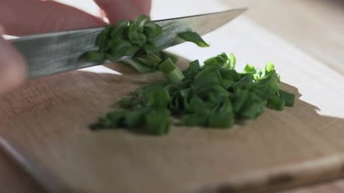 Loopable clip of woman cutting green onion on the kitchen with knife, close up view
