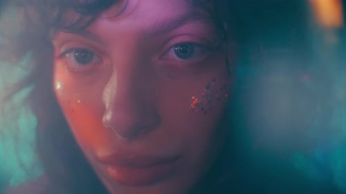 Portrait of Beautiful Girl with Glitter on Her Face in Soft Colorful Lighting