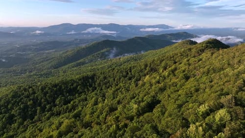 Beautiful mountain landscape with green hills and blue sky. Aerial wide shot. Flying clouds and fog