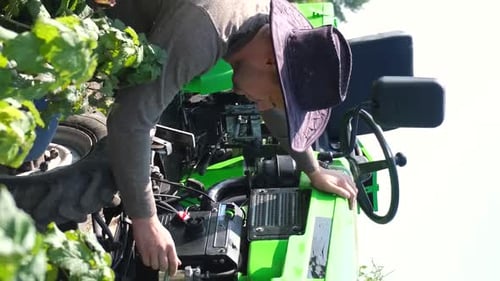 Ein junger Landwirt repariert einen Minitraktor inmitten eines Feldes, Landarbeiter, Vertikales Video