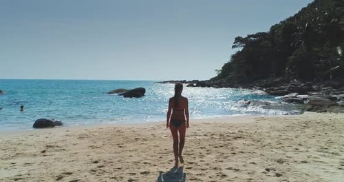 Woman Walking Along Sandy Beach Near Clear Blue Water on a Sunny Day