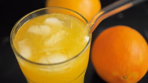 close-up of a glass filled with orange juice and ice cubes on the surface of the cocktail. Using reu