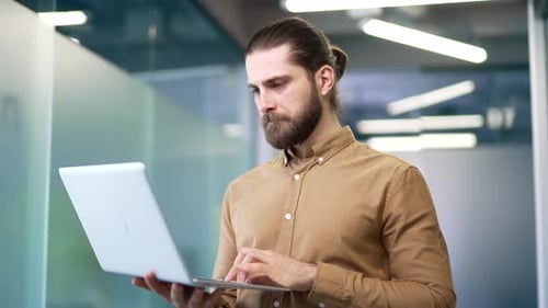 Portrait of smiling businessman using a laptop computer standing at workplace in business office.