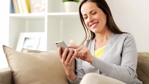 Woman using smartphone on sofa at home