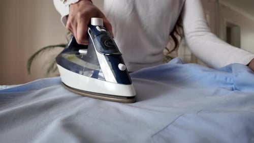 Close up woman ironing a blue shirt at home with white steam