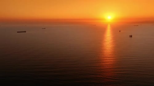 Pacific Ocean lit with orange light of setting sun. Trade ships are standing on the anchor.