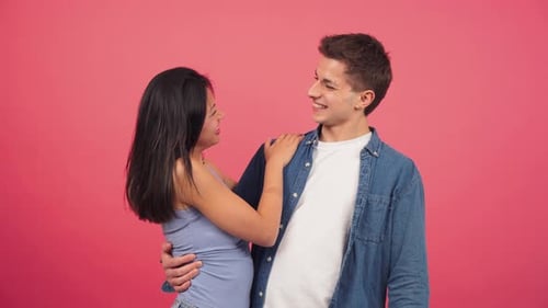 Young Adult Multiracial Couple Smiling and Hugging in Front of a Red Color Studio Background Two