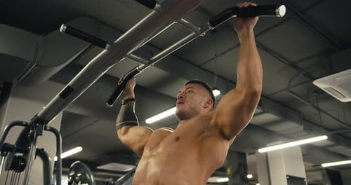 Side View of a Young Athlete with a Naked Torso Who Performs Pullups While in the Gym
