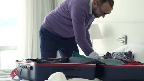 Man Packing Suitcase with Clothes in Hotel Room