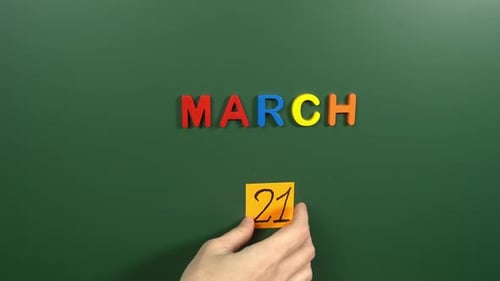 Hand sticking a sticker 21 March calendar day on school board. 21 date of March. Twenty first day