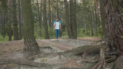 Junger Mann mit Rucksack, Wanderer, der im Wald steht, schaut sich um, lächelt im Sonnenlicht, Natur allein