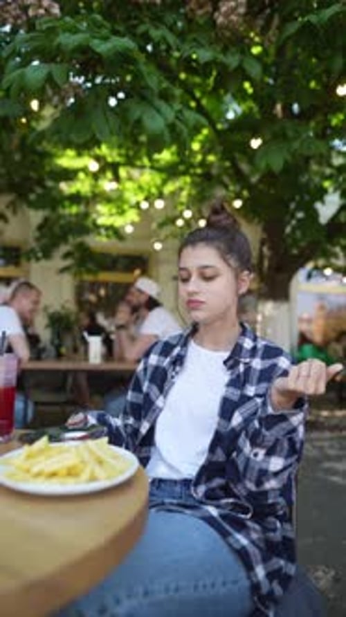 With a Café Terrace As the Backdrop a Pretty Girl is Enjoying French Fries During the Summer