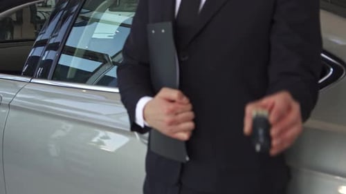 Sales Manager Proudly Presents a Key Beside a Sleek Car