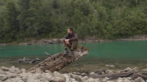 Man Sitting on Log by River in Nature
