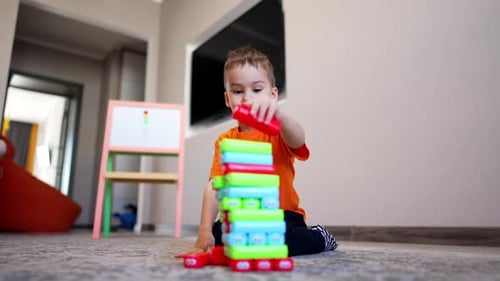 Concentrated Caucasian toddler sits on the floor building a tower.