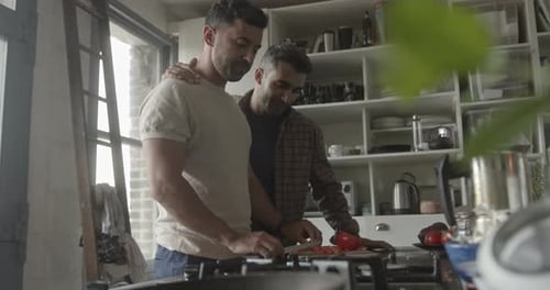 Pareja de hombres hispanos cocinando en la cocina y mirando el teléfono inteligente