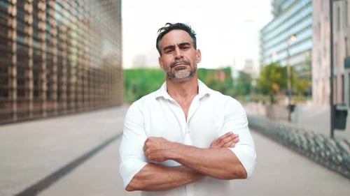 Mature businessman stands with his arms crossed and looks into the camera