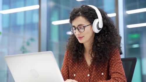 Woman with Headphones Works at Laptop in Office