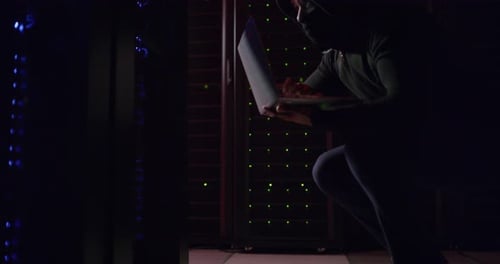 Hooded Hacker with Laptop in Dark Server Room