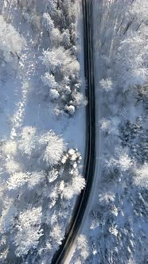 Aerial View of Scenic Road Through Snowy Winter Mountain Forest