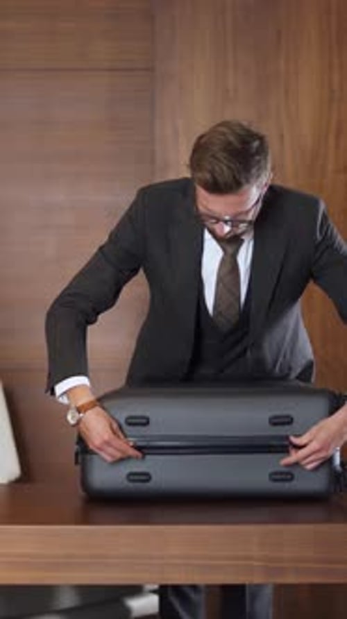 Jovem empresário de terno fecha a mala com coisas e a leva embora, viagem de negócios, quarto de hotel