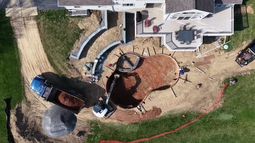 Backyard pool construction in a US suburban neighborhood, showing excavator, dump truck,