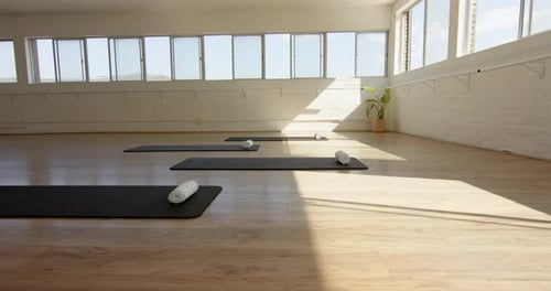 A yoga studio is bathed in natural light, with mats and bolsters neatly arranged, with copy space