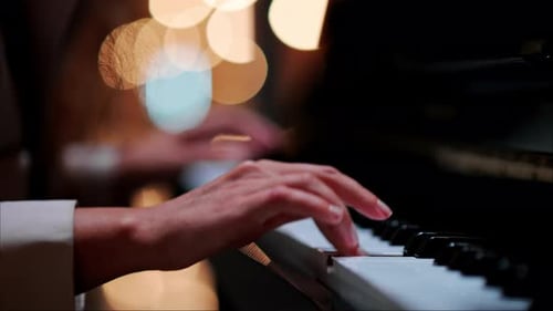 Close up of a woman's hands playing the piano with blurry lights on the background