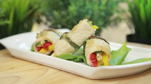 El chef sirve y presenta rollitos de filete de pollo horneados con verduras en un plato blanco