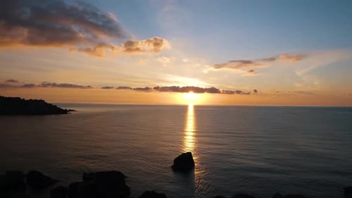 Fantastic sun setting on the ocean from a rocky shore, with small clouds and majestic colours, a fis