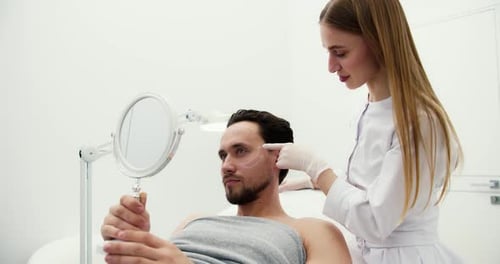 Hübscher Mann bei Beratung beim Chirurgen oder Kosmetiker mit Gesichtskonturierung und Blick in den Spiegel