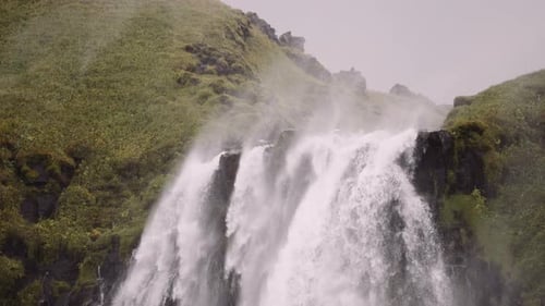 Powerful Waterfall Flowing Over Green Mountain Cliff