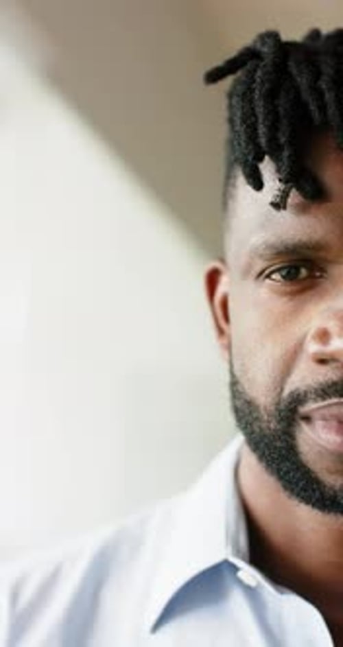 Vertical video: Smiling man with dreadlocks wearing light blue shirt, close-up portrait
