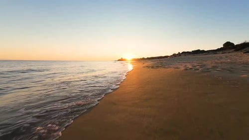Golden Sunset Reflecting on Calm Ocean Waves Along Sandy Shore