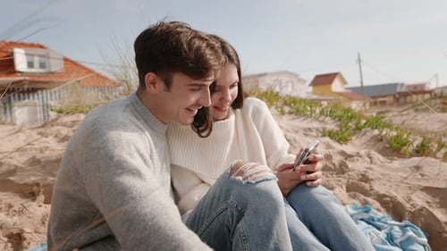 Young Couple Sharing a Moment on Sandy Beach with Smartphone