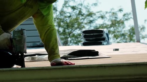 Construction Worker Uses Nail Gun on Roof Shingles