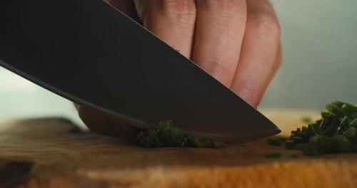 Close shot of a male hand cutting chives on a wooden cutting board in a smoky kitchen atmosphere